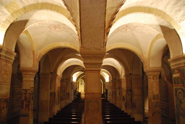 Crypt with cross vaults, frescoed columns and wooden pews under warm light