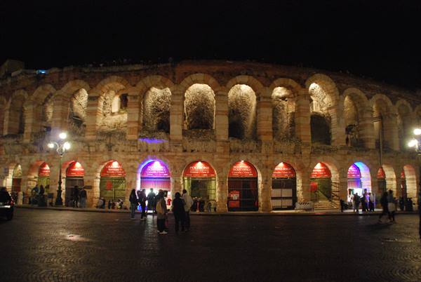 Verona's Roman Arena at night, illuminated stone arches, people strolling in the square