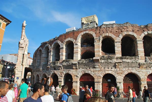 Tourists stroll past the great stone arches of Verona's Arena