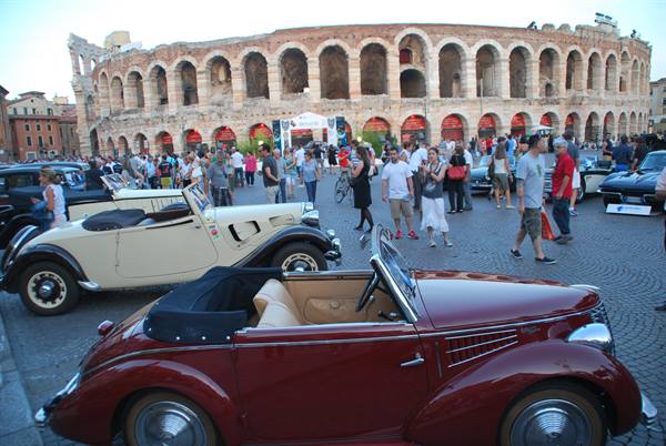 Vintage convertible cars on cobblestones in front of Verona's Arena crowded with visitors