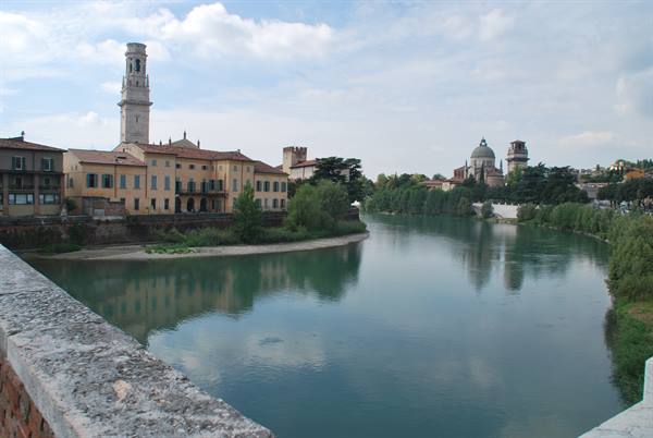The Adige river flows past Verona's Duomo buildings under a cloudy sky