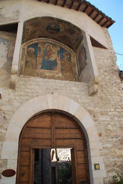 Medieval fresco above wooden portal on pale stone building, sunlight