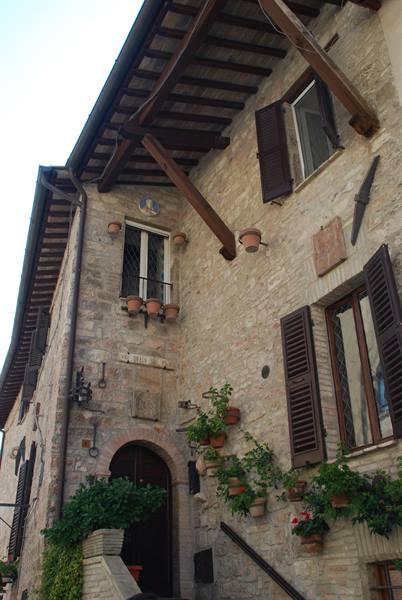 Stone house with wooden beams, dark shutters and hanging flower pots, Assisi