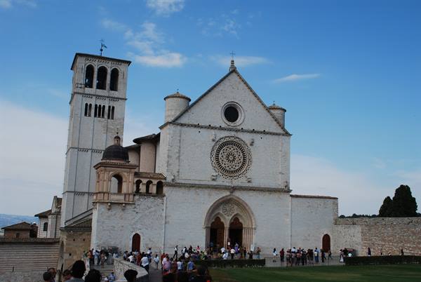 White facade of the Basilica of Saint Francis in Assisi with rose window and tourists