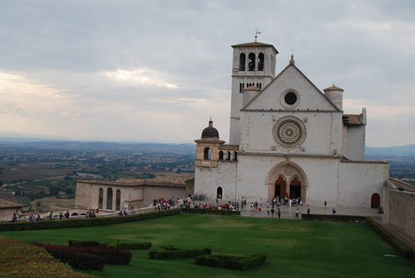 Basilica of San Francesco in Assisi, white facade with rose window, visitors on the lawn