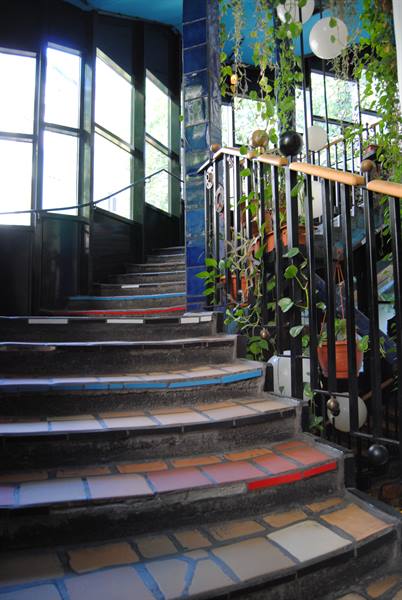 Stairs of colorful ceramic tiles with black railing and hanging plants, Hundertwasserhaus