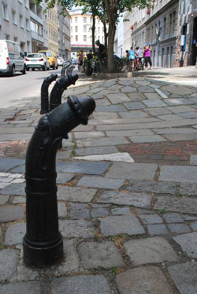 Old black cast-iron water pumps on cobblestones, cyclists and pedestrians on Vienna streets