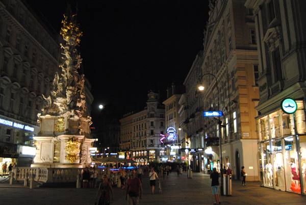 Night on Vienna's Graben: the illuminated Plague Column among glowing shop windows