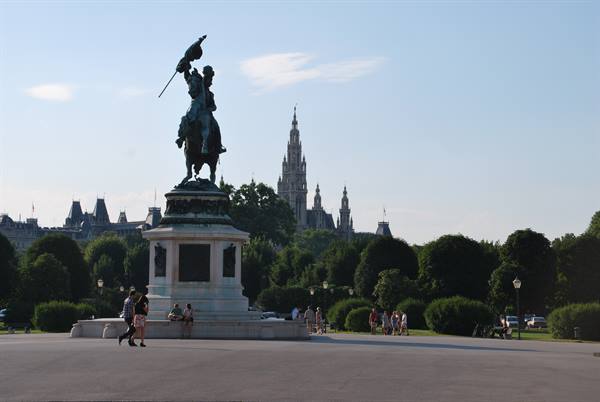 Bronze equestrian statue in Vienna, with the Rathaus and strolling tourists