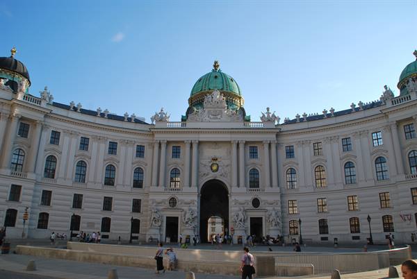 White Hofburg facade in Vienna with green dome and tourists strolling below