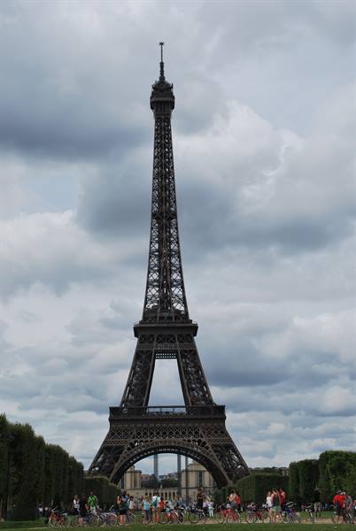 Cyclists gathered beneath the Eiffel Tower under a cloudy sky