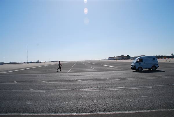 Person walks across airport tarmac, white van parked, clear blue sky