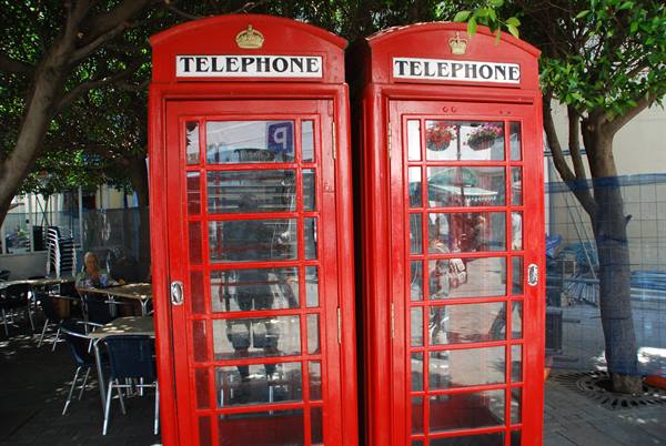 Two red English-style telephone booths standing among trees and outdoor café