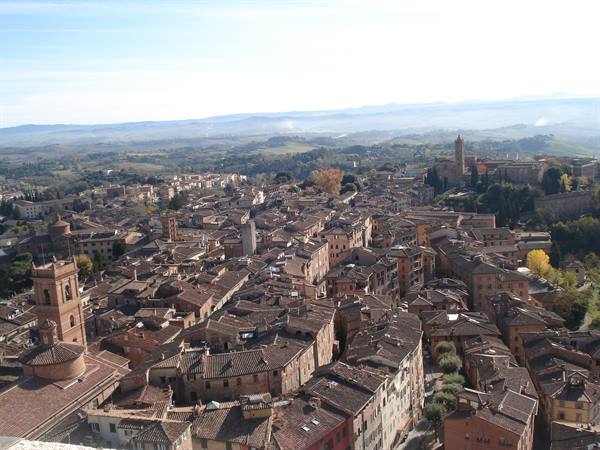 Siena's terracotta rooftops seen from above, hazy Tuscan hills beyond