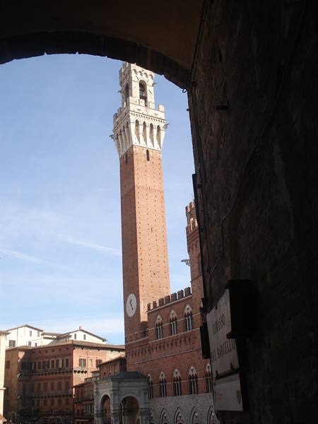 Torre del Mangia framed by a dark arch, red brick tower against blue sky in Siena