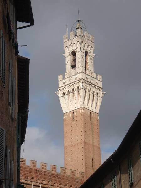 Torre del Mangia in Siena, brick and travertine tower among medieval buildings, cloudy sky