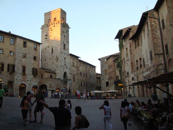 Tourists in San Gimignano's Piazza della Cisterna, medieval tower lit by sunlight