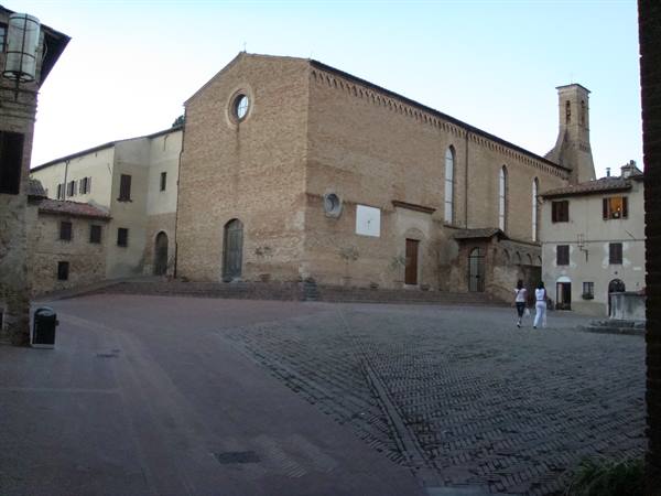 Brick church with bell tower on cobbled square in San Gimignano