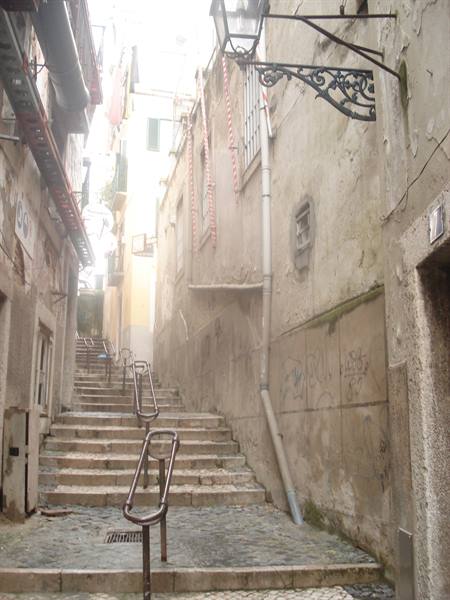 Narrow stepped alley with worn walls, metal handrails and wrought-iron street lamp