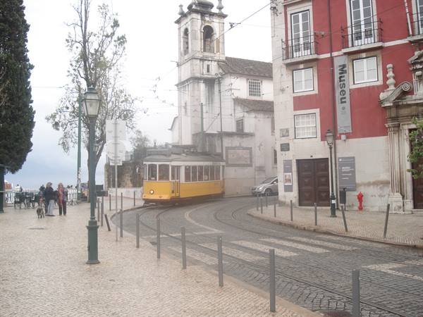 Yellow tram curving on tracks in Lisbon, church and colorful buildings, grey light