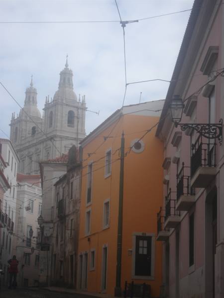 Steep street with colorful houses, tram wires and baroque church towers, Alfama, Lisbon