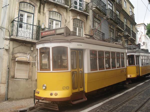 Yellow tram stopped on tracks beside old tiled buildings in Lisbon