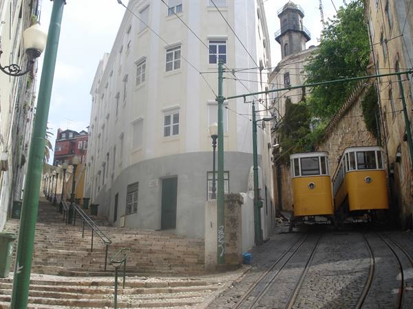 Yellow funicular climbing a steep Lisbon street beside stone steps