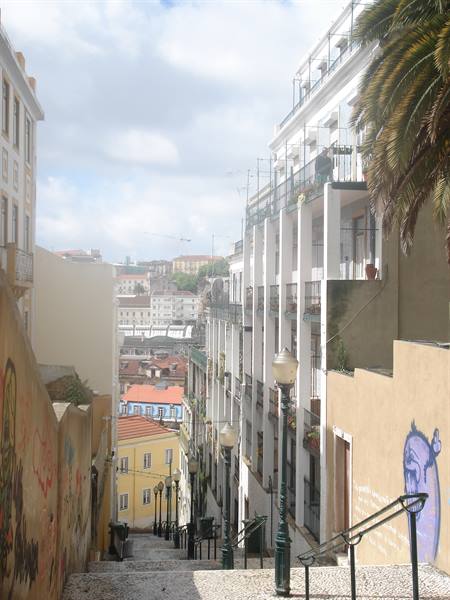 Tiled staircase between yellow and white buildings in Lisbon, palm trees and lampposts