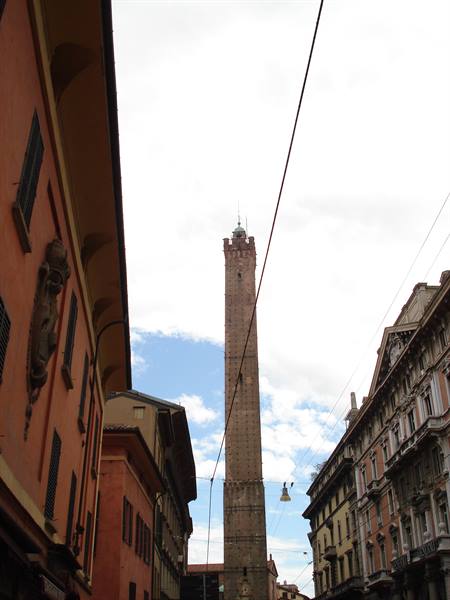 Brick Asinelli Tower rising between ochre palaces and electric wires, cloudy sky