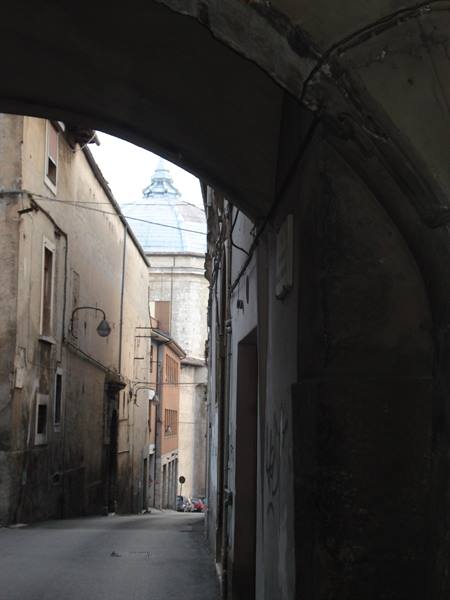 Narrow street between old stone houses under an arch, dome in background