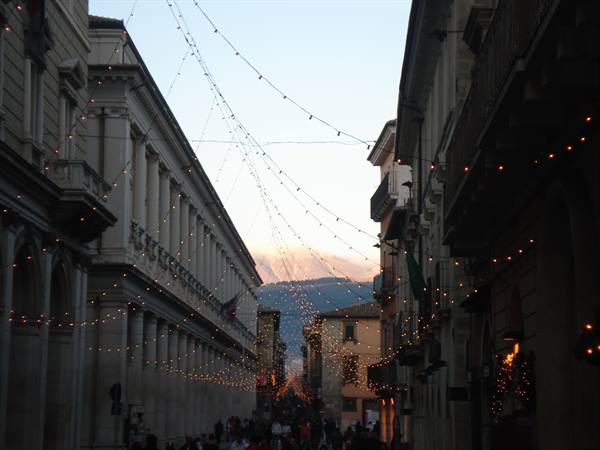 Christmas lights strung across old buildings, crowd below, mountains in the distance
