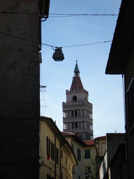 Lucca cathedral bell tower rising between houses against blue sky
