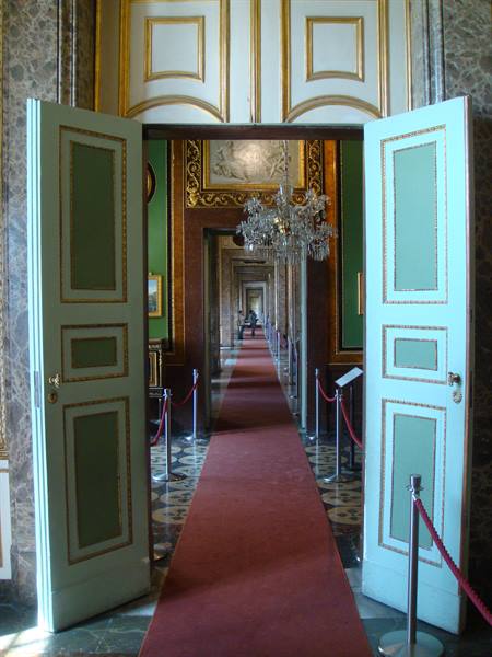 Pale blue doors open onto a long gallery with red carpet and crystal chandelier