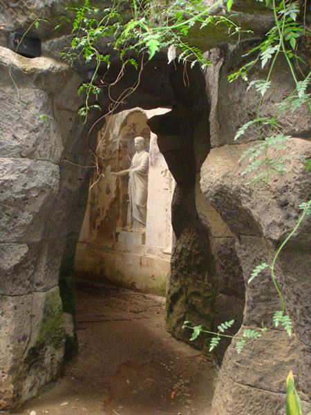 Statue framed by tuff rocks and greenery in Syracuse grotto
