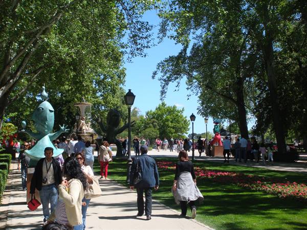 Tree-lined paths of Retiro Park in Madrid with sculptures, fountain and visitors