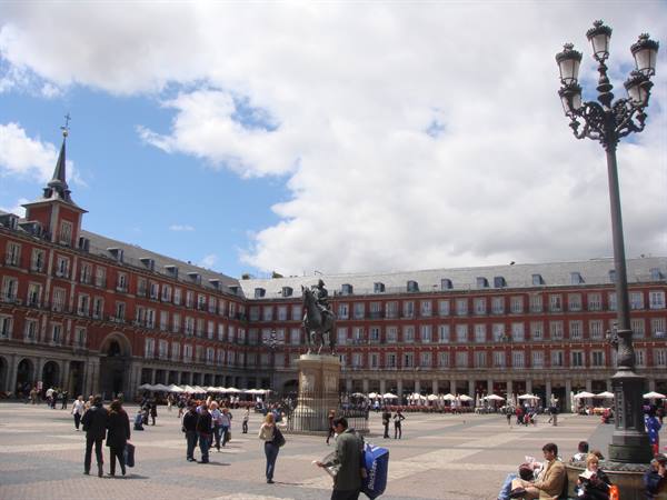 Tourists under lampposts at Plaza Mayor, Madrid, equestrian statue among brick buildings