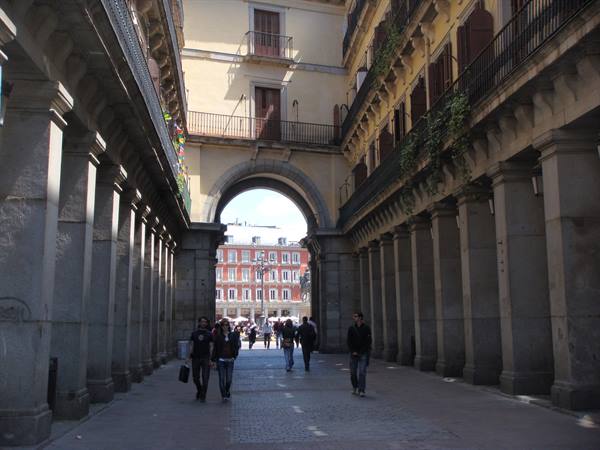 Stone arcades with archway and strolling people, Plaza Mayor in Madrid