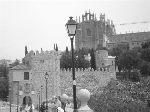 Stone walls and crenellated tower in Toledo, lamppost, Gothic monastery behind, tourists
