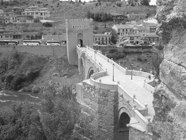 Alcántara Bridge in Toledo, stone arches and gate tower amid the hills