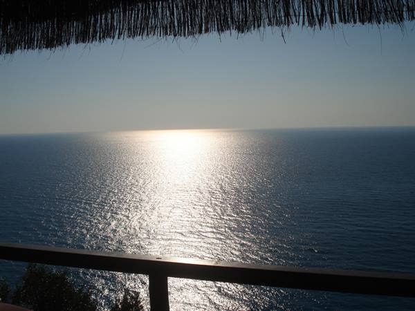 From thatched-roof terrace, sunlight reflects across the calm sea