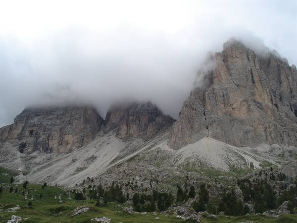Dolomite rock walls wrapped in clouds above scree slopes and green meadows
