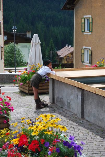 Child in hat and boots leans on a wooden fountain surrounded by flowers