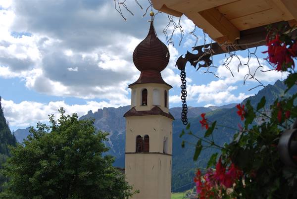 Onion-domed bell tower framed by a wooden balcony and red flowers, Dolomites