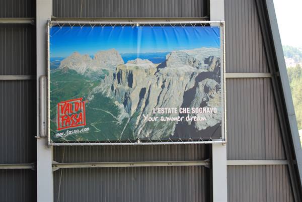 Val di Fassa tourist banner showing Dolomite peaks, hung on a metal wall