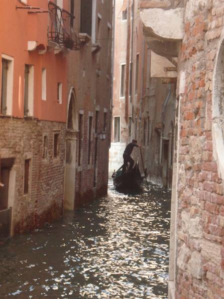 Gondolier rowing through a narrow canal between brick houses in Venice