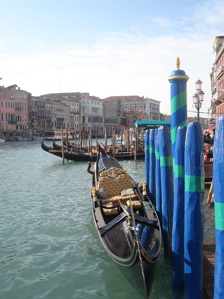 Black gondola with golden seats moored to blue poles in Venice