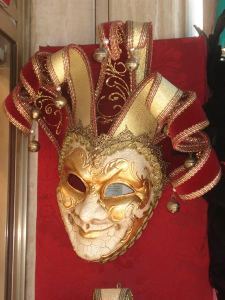 Golden Venetian jester mask in papier-mâché and red velvet displayed in a shop