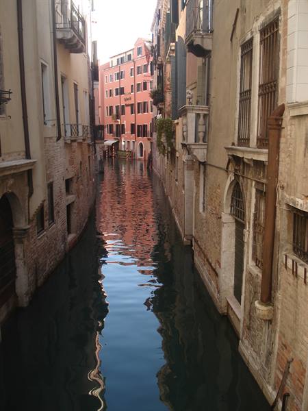 Narrow canal between brick and plaster buildings, still water reflecting facades