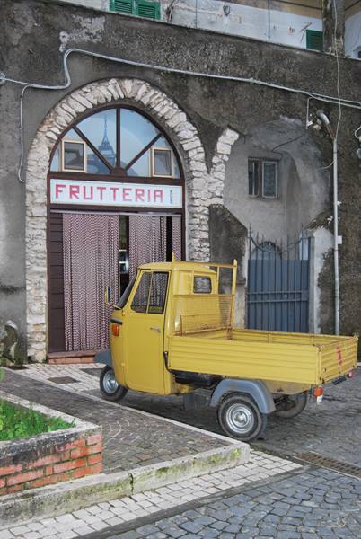 Yellow Piaggio Ape parked outside a frutteria with red sign