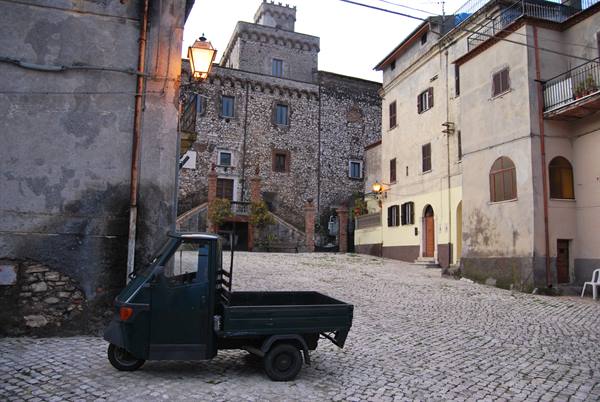 Green Piaggio Ape parked on a cobbled alley in front of a stone castle